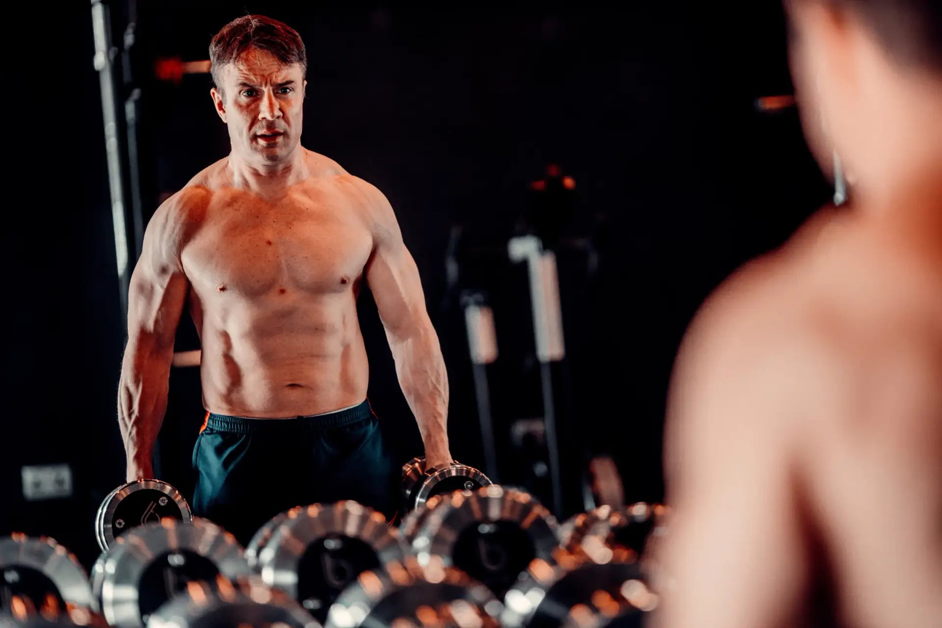 BTX client standing behind the dumbbell rack in the studio