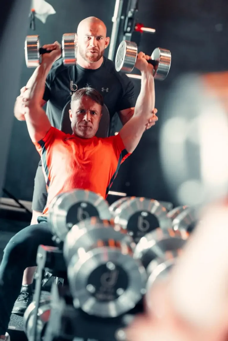 BTX coach spotting a client through a seated dumbbell shoulder press at the Finchley Road studio